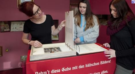 Ausstellungsraum iim Schreiber-Museum: Drei Frauen betrachten einen großen Ordner mit Bildern.