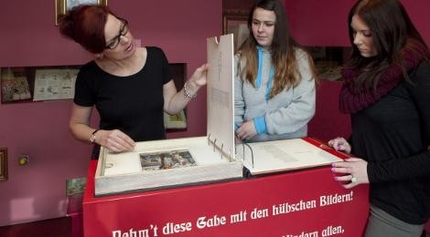 Ausstellungsraum iim Schreiber-Museum: Drei Frauen betrachten einen großen Ordner mit Bildern.