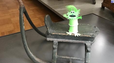 Ein gebasteltes kleines Monster steht auf einem alten Schlitten im Stadtmuseum.