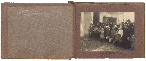 Aufgeschlagenes altes Fotoalbum: Ein eingeklebtes Foto zeigt Erwachsene und viele Kinder mit Gefäßen, die Schlange stehen.