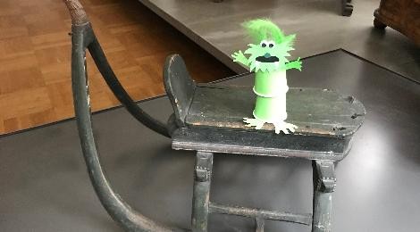 Ein gebasteltes kleines Monster steht auf einem alten Schlitten im Stadtmuseum.
