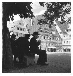 Der Marktplatz in Esslingen. Im Vordergrund sitzen drei Männer mit Hut auf einer Bank im Schatten unter einem Baum.