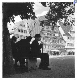 Der Marktplatz in Esslingen. Im Vordergrund sitzen drei Männer mit Hut auf einer Bank im Schatten unter einem Baum.
