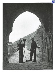 Unter dem Torbogen des Neckarhaldentörles stehen zwei Kaminkehrer in Berufskleidung und mit Ausrüstung. Sie lächeln in die Kamera, einer hebt grüßend einen Zylinderhut. Im Hintergrund der Weg und der Weinberg.