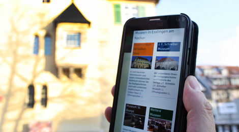 Eine Hand hält ein Smartphone, im Hintergrund das Stadtmuseum im Gelben Haus.