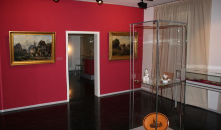Ausstellungsraum mit Vitrine und zwei Gemälden an der Wand.