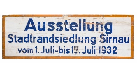 Das Schild aus Holz ist drei Meter breit und einen Meter hoch. Es trägt die Beschriftung: "Ausstellung Stadtrandsiedlung Sirnau vom 1. Juli bis 17. Juli 1932"