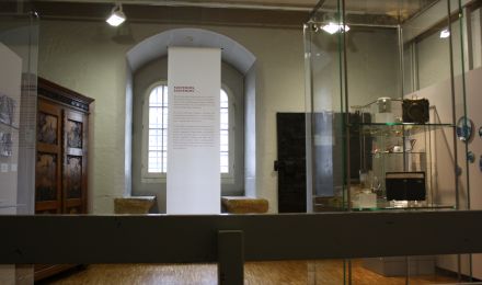 Ausstellungsraum: Im Vordergund Vitrinen, im Hintergrund ein großer alter Schrank.