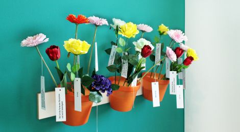 Installation: Blumentöpfe mit verschiedenfarbigen Papierblumen. An jeder Blume hängt ein kleines Papierschild.