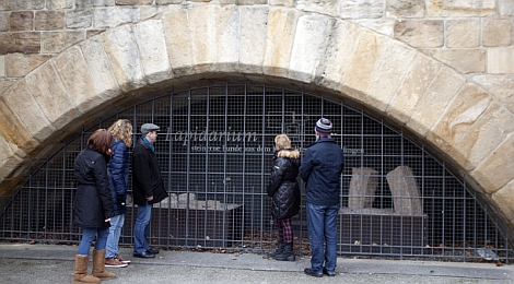 Vor einem großen steinernen Bogen der Inneren Brücke: Interessierte Personen betrachten ausgestellte Steinfragmente hinter einem Gitter. Darüber befindet sich die Beschriftung "Lapidarium". 