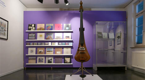 Ausstellungsraum mit Elektrobasse und Schallplatten auf einem Regal im Hintergrund.