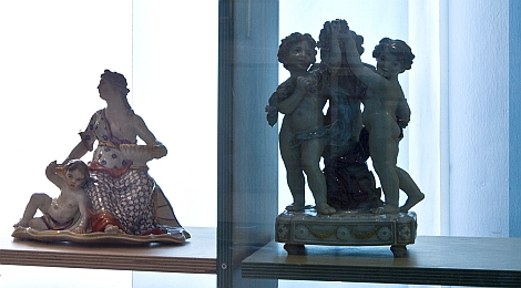 In einer Vitrine: 2 Porzellangruppen: links: Dame mit Putto, rechts: drei tanzende Putten.
