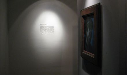 Ausstellungsraum mit einem Gemälde und einer Infotafel.