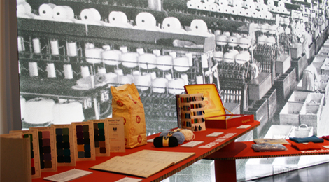 Podest mit Objekten zur "Esslinger Wolle": Mmusterkarten, Wolknäuel, eine Papiertüte voller Wollknäuel. Im Hintergrund ein großes Foto von einer Fabrikhalle.