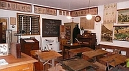 Schulmuseum Sulzgries: Im Schulzimmer stehen Reihen von alten Schulbänken und das Lehrerpult. An der Wand hängen Schultafeln.