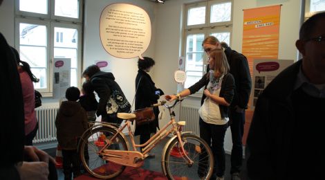 Ausstellungsraum: Besucherinnen und Besucher betrachten ein Fahrrad.